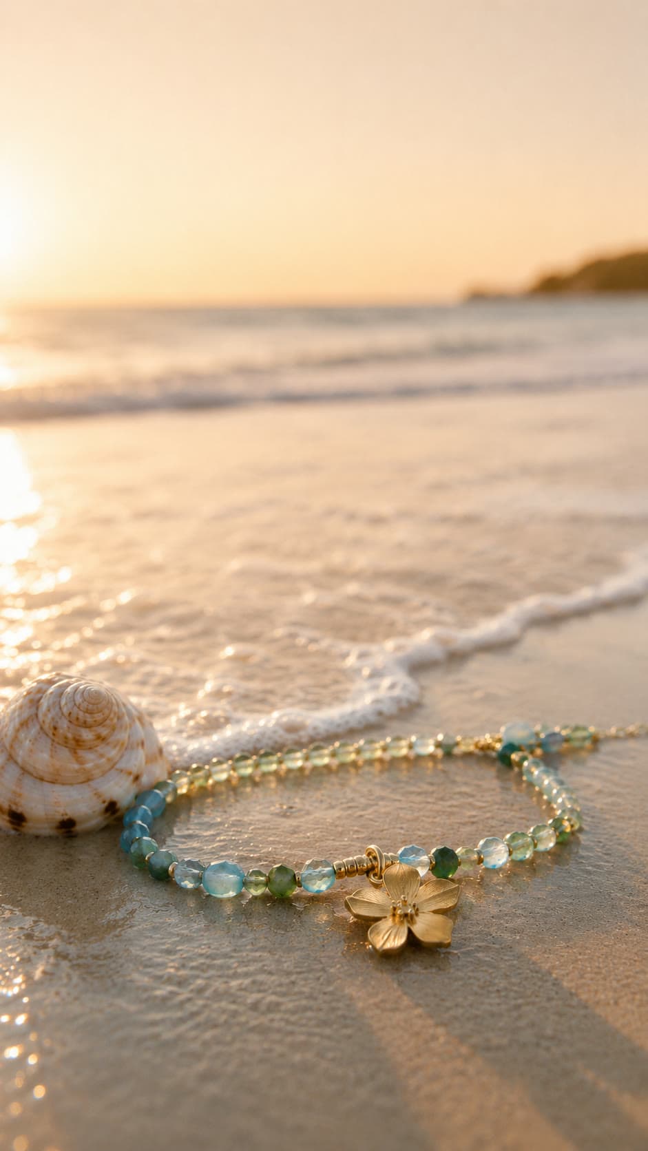 Collar de aguamarina y jade con dije de flor dorada sobre la arena al atardecer