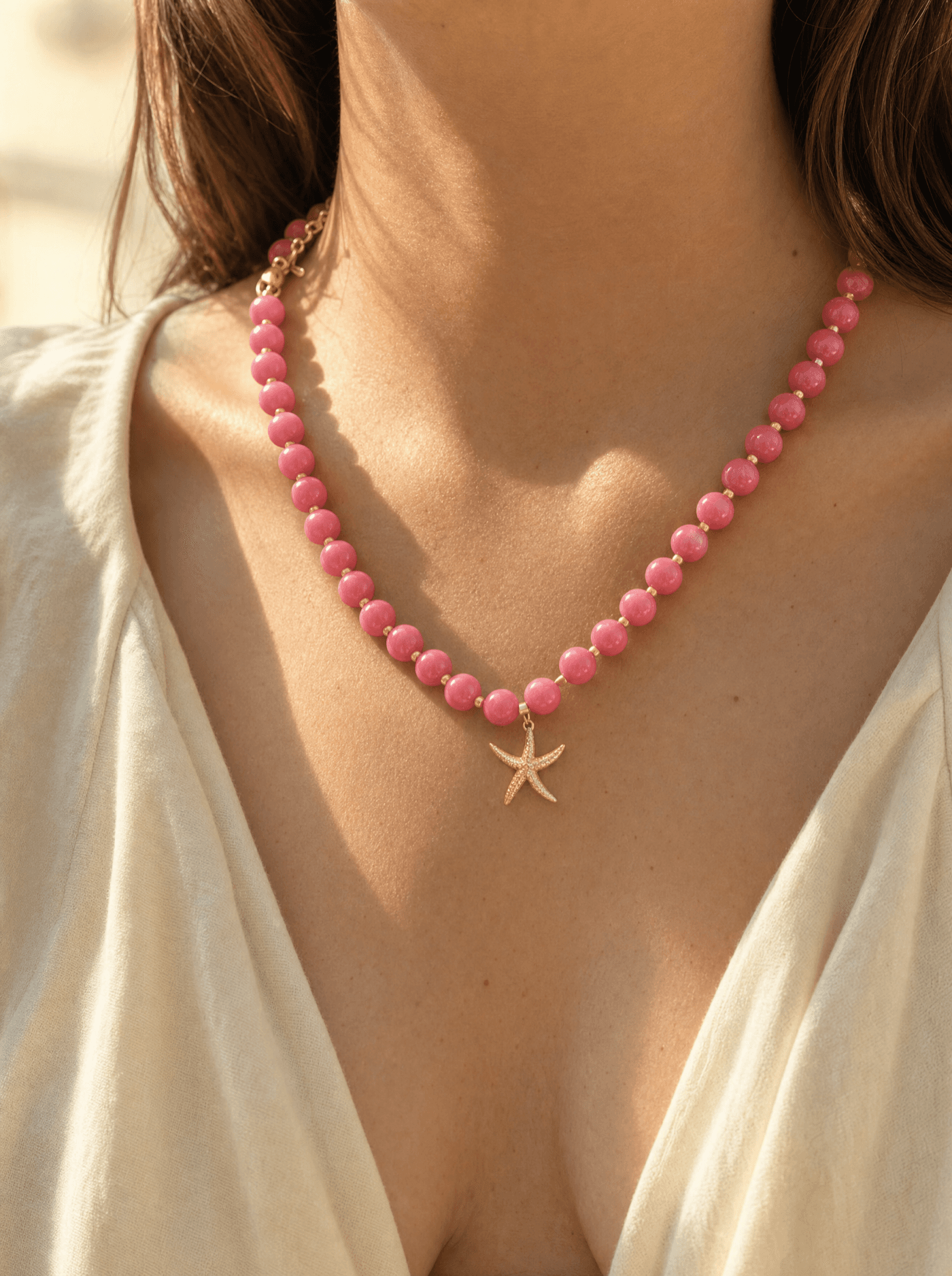 Collar de cuentas de ágata rosada con dije de estrella de mar dorada sobre cuello de mujer.