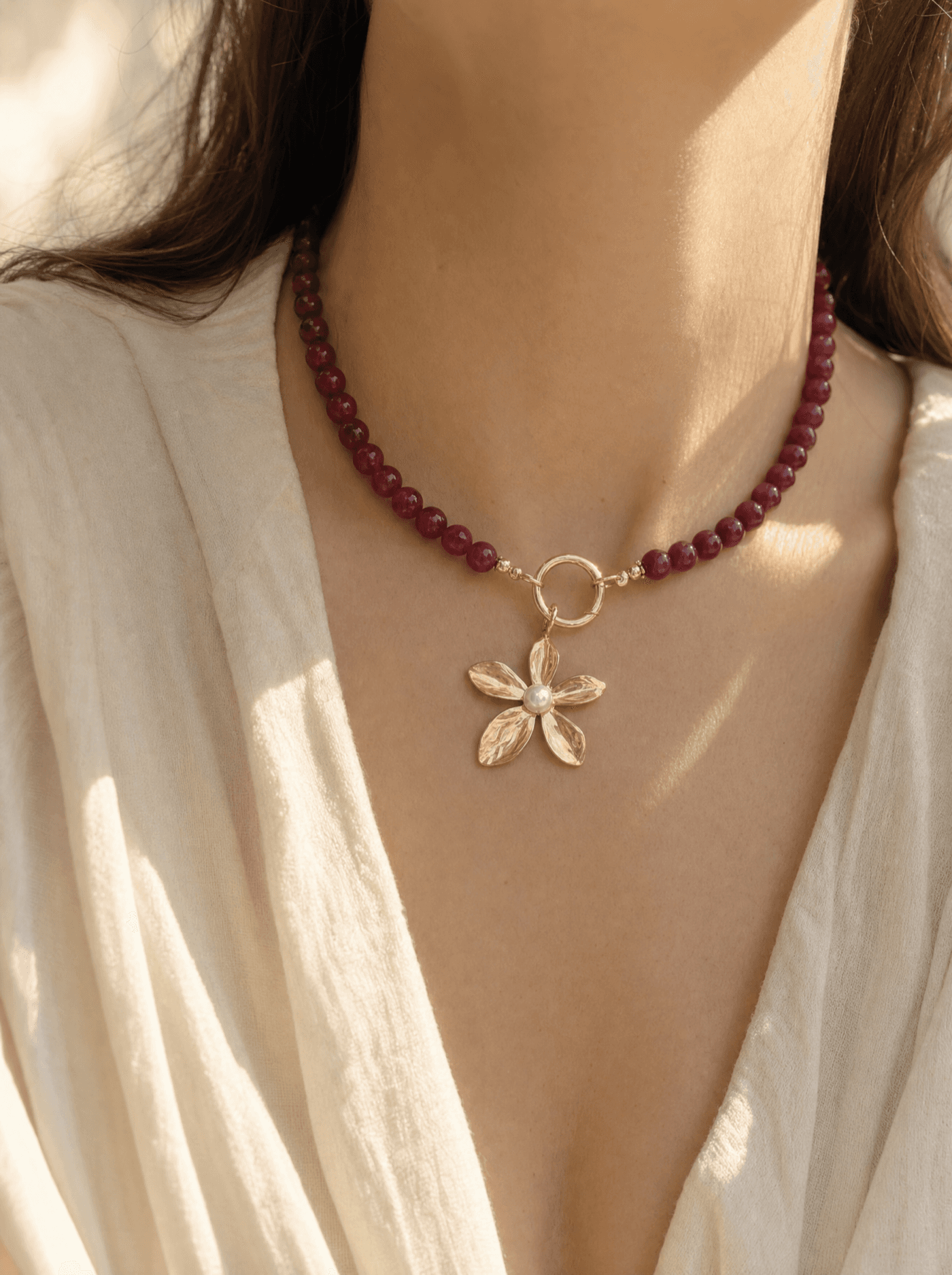 Collar de cuentas de ágata roja con dije de flor dorada sobre cuello de mujer.