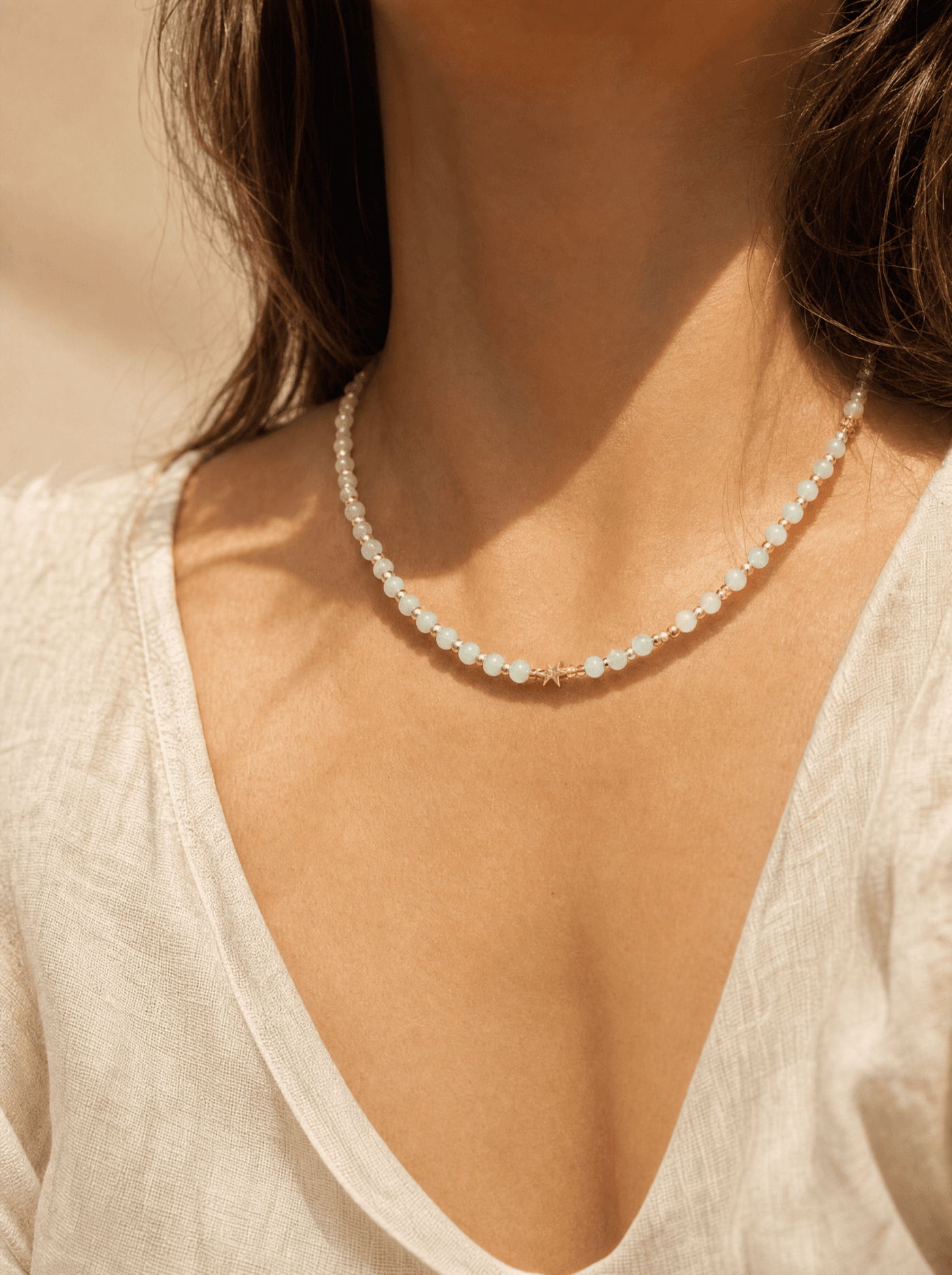 Collar largo de cuentas de amazonita verde pálido con acentos dorados sobre cuello de mujer.