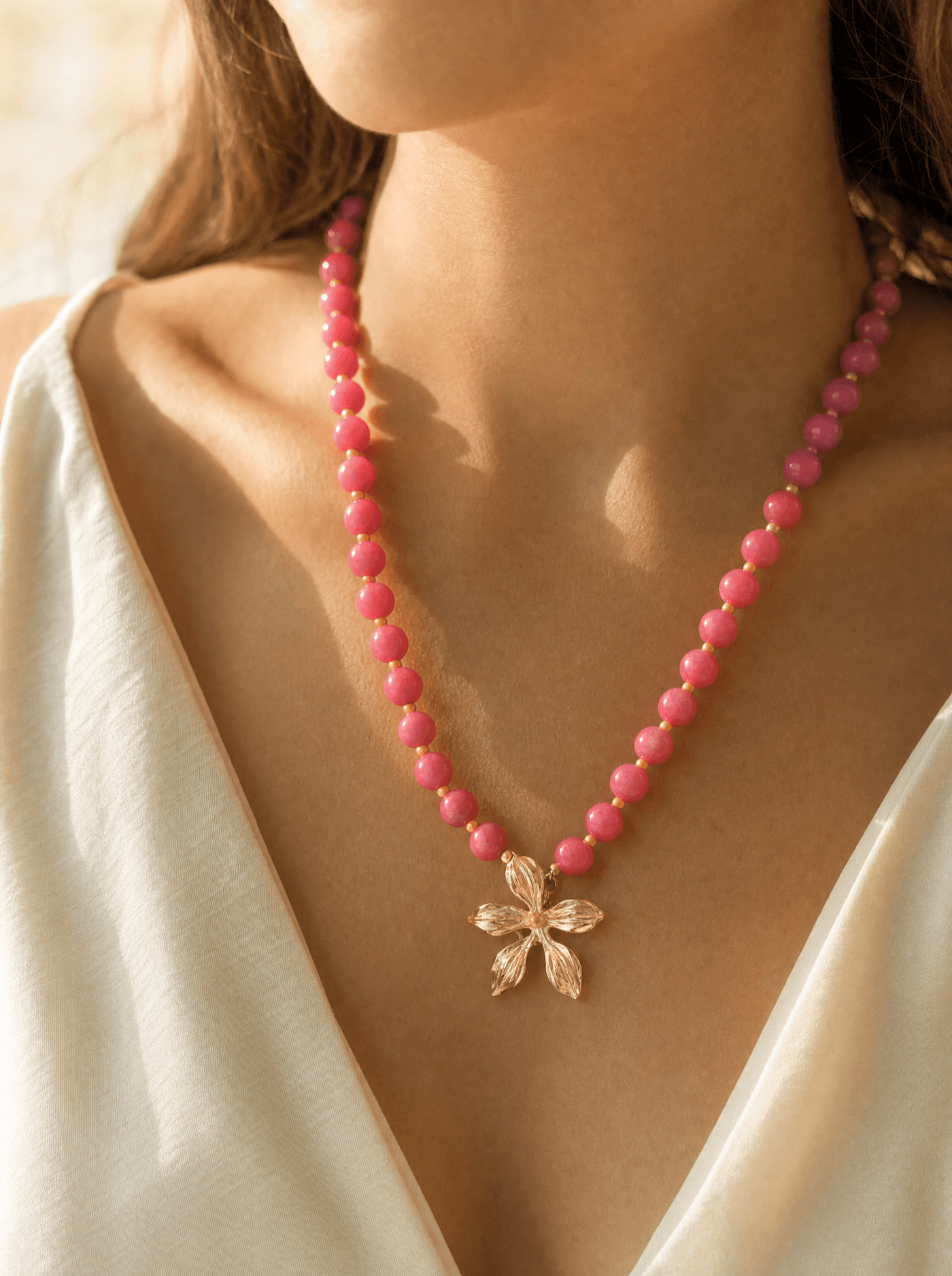 Collar de cuentas de ágata rosada con dije de flor dorada sobre cuello de mujer.
