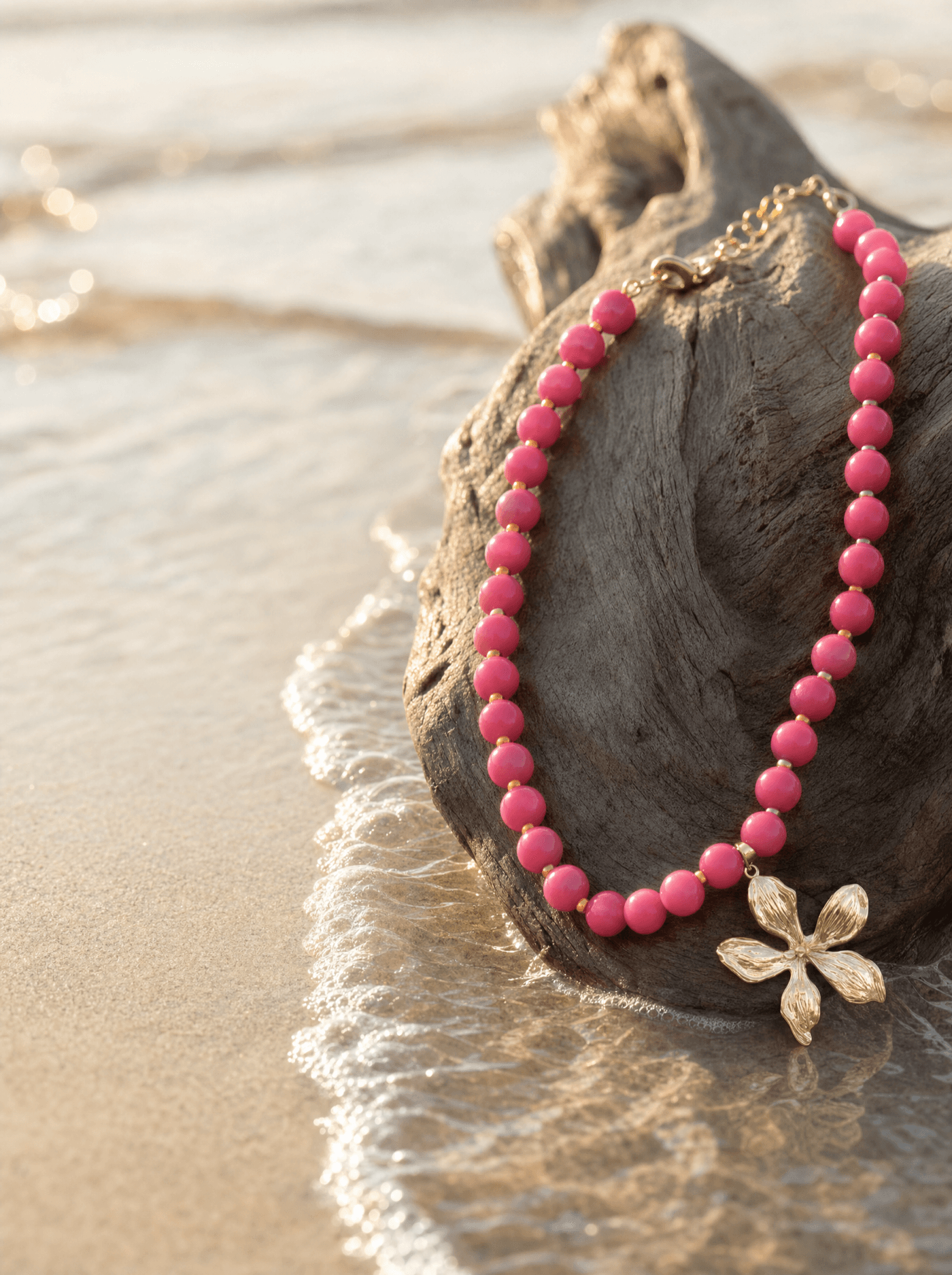 Collar de ágata rosada sobre madera de deriva a la orilla del mar al atardecer.