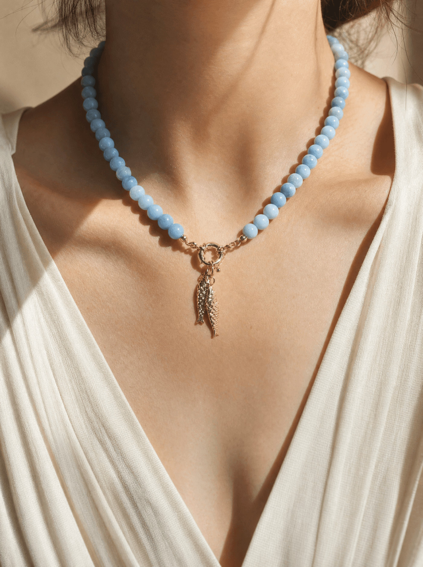 Collar de cuentas de jade azul celeste con dije de hojas doradas sobre cuello de mujer.