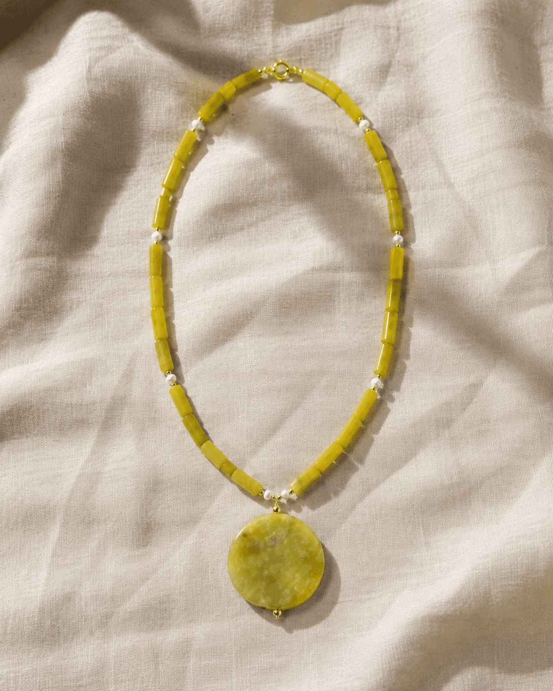 Collar Lima completo extendido sobre lino marfil, mostrando los tubos de jade y el medallón.