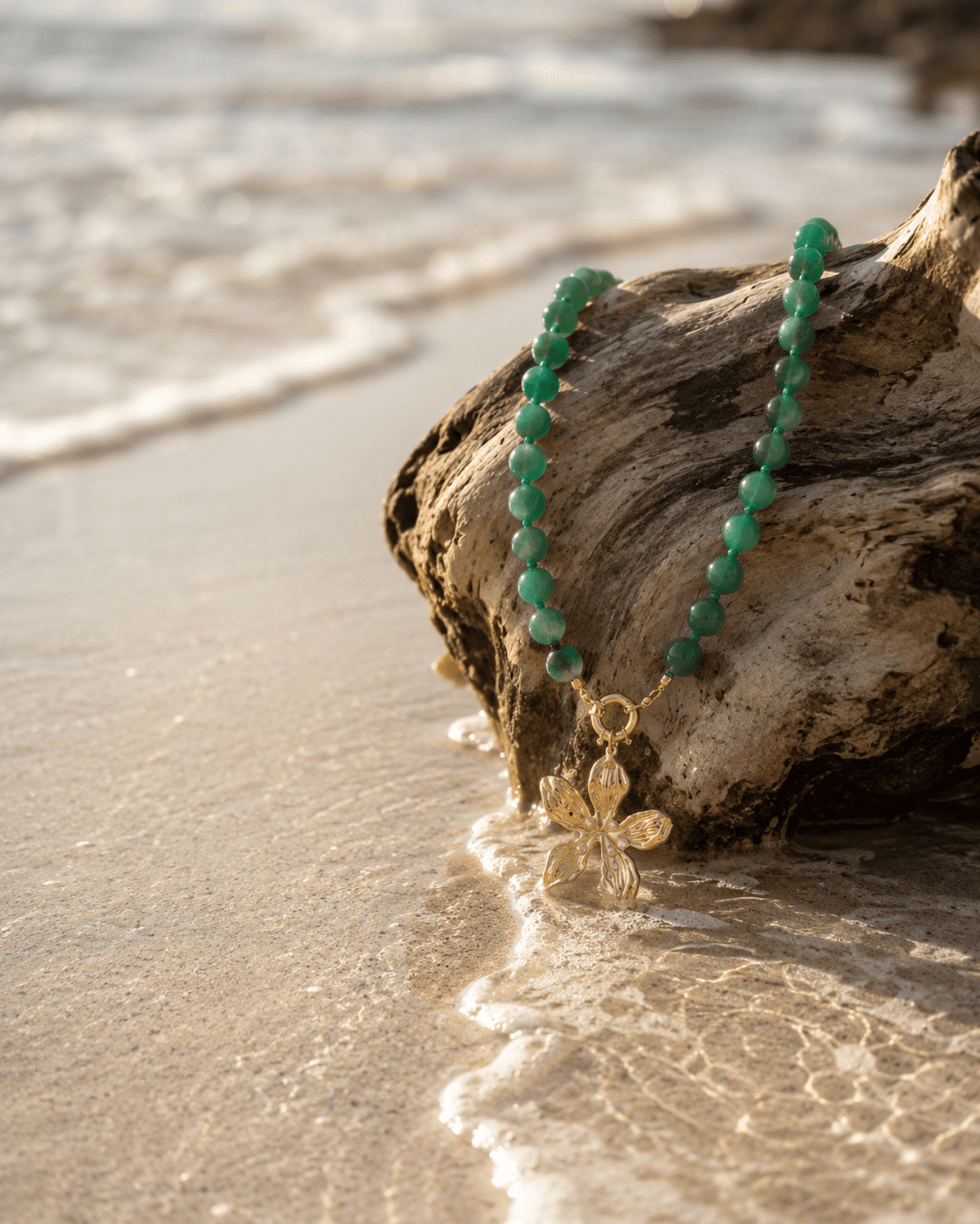 Collar de aventurina verde sobre madera de deriva a la orilla del mar al atardecer.