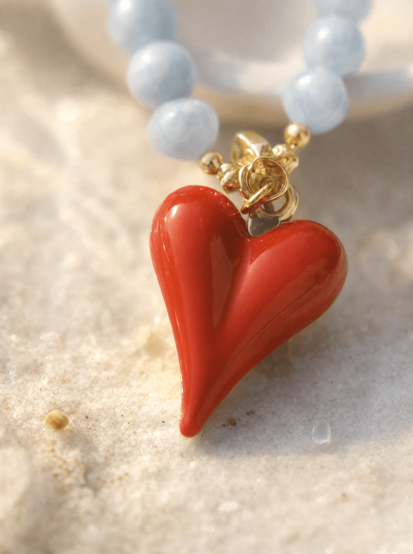 Detalle macro del corazón rojo de vidrio soplado con casquillo dorado junto a las cuentas de aguamarina.
