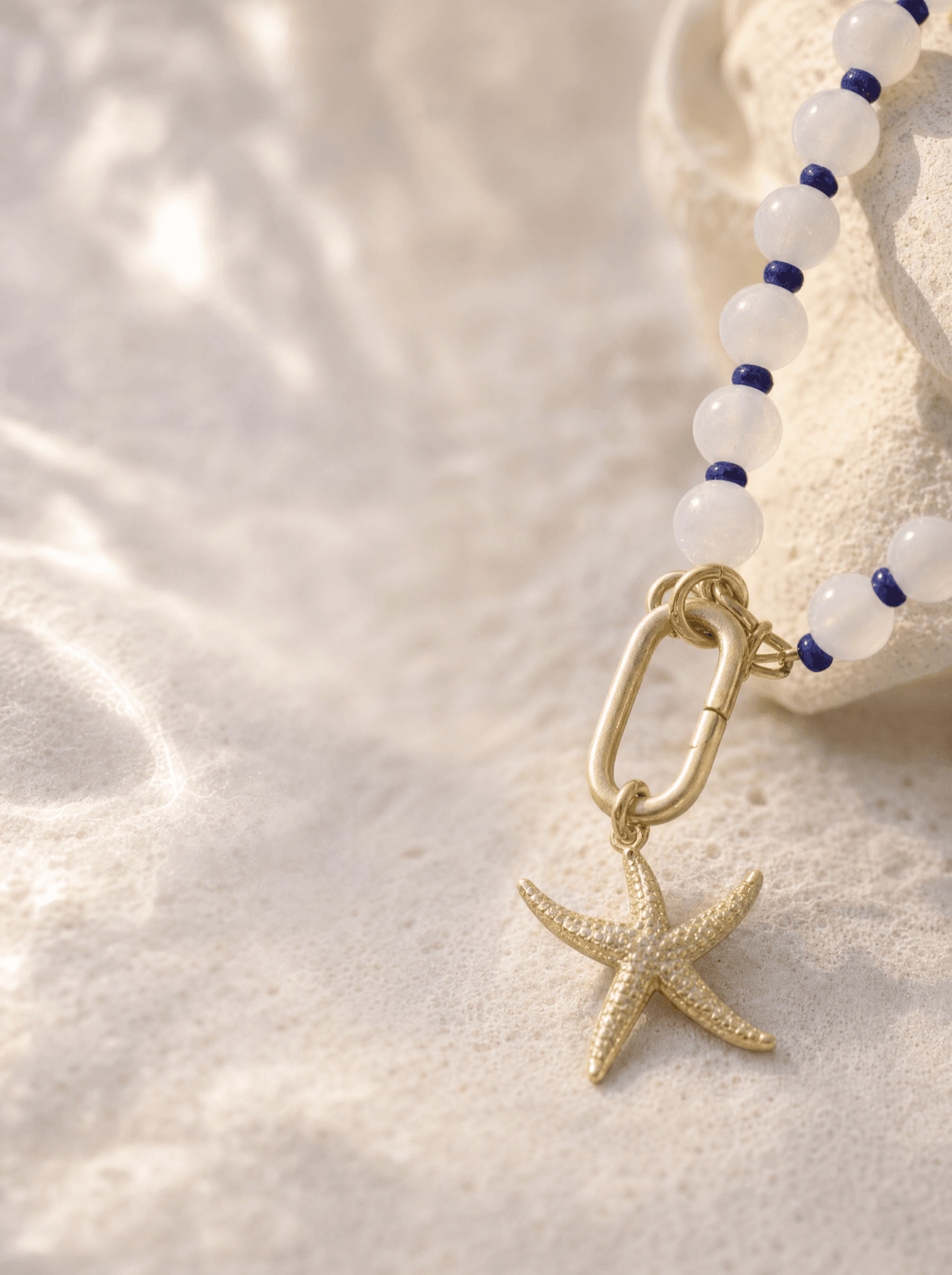 Detalle macro del dije de estrella de mar en baño de oro y el eslabón oval dorado junto a las cuentas.